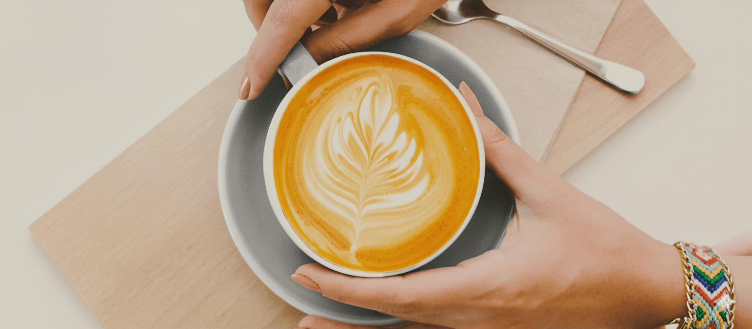 Hands holding a rooibos latte with latte art